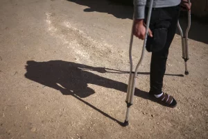 كان سليمان خليل منهمكاً في قطف الزيتون داخل بستان سوري، مع اثنين من أصدقائه قبل أربعة أشهر، دون أن يدرك أن التربة تحت أقدامهم لا تزال تخفي بقايا الحرب القاتلة. فجأة، لاحظ الثلاثة لغماً أرضياً ظاهراً على الأرض. انتابت حالة من الذعر الأصدقاء الثلاثة، وحاولوا مغادرة المكان سريعاً، لكن قدم خليل وطأت بالخطأ لغماً أرضياً فانفجر. ركض أصدقاؤه مرعوبين للبحث عن سيارة إسعاف، بينما ظن خليل، 21 عاماً، أنهم قد تركوه. قال خليل لوكالة «أسوشييتد برس»: «دأت بالزحف، ثم انفجر لغم ثانٍ»، مضيفاً: «في البداية، ظننت أنني متّ. لم أعتقد أنني سأنجو من هذا الموقف». أُصيب خليل في ساقه اليسرى إصابة بالغة في الانفجار الأول، بينما بُترت ساقه اليمنى من فوق الركبة في الانفجار الثاني. واستخدم قميصه لربط الجرح، وصرخ طلباً للمساعدة حتى سمعه جندي قريب وهرع لإنقاذه. قال خليل: «مرت علي أيام فقدت فيها رغبتي في الحياة». كان جالساً على فرشة رقيقة، وساقه المبتورة لا تزال ملفوفة بقطعة قماش بيضاء بعد أربعة أشهر من الحادث. خليل، من قرية قميناس في جنوب محافظة إدلب، مرتبط بعلاقة خطوبة، ويأمل في الحصول على طرف صناعي، ليعود إلى العمل، ويعول عائلته. رغم أن الحرب السورية التي استمرت نحو 14 عاماً انتهت بسقوط بشار الأسد في الثامن من ديسمبر (كانون الأول)، فإن بقايا الحرب لا تزال تفتك بالناس قتلاً، وتشويهاً. وتكشف الأرقام الصادرة عن منظمة «آي إن إس أو»، المعنية بالسلامة، أن الألغام والمتفجرات قتلت ما لا يقل عن 249 شخصاً، بينهم 60 طفلاً، وأصابت 379 آخرين منذ الثامن من ديسمبر، تاريخ سقوط نظام الأسد. استخدمت القوات الحكومية السورية وحلفاؤها، إلى جانب جماعات من المعارضة المسلحة، الألغام منذ عام 2011، ما أدى إلى تلوث مساحات شاسعة بها، كثير منها لم يكن متاحاً الدخول إليها سوى بعد انهيار حكومة الأسد، الأمر الذي تسبب في تفاقم أعداد ضحايا الألغام، وفقاً لتقرير حديث صادر عن منظمة «هيومان رايتس ووتش». يذكر أنه قبل الثامن من ديسمبر، كانت الألغام وبقايا الحرب تتسبب كذلك في إصابات ووفيات متكررة للمدنيين العائدين إلى منازلهم، أو إلى أراضيهم الزراعية. في هذا الصدد، قال ريتشارد وير، كبير الباحثين بمجال الأزمات والصراعات لدى «هيومان رايتس ووتش»: «دون جهود تطهير عاجلة على مستوى البلاد، سيكون هناك المزيد من المدنيين العائدين لاستعادة حقوقهم وحياتهم وسبل عيشهم، وأراضيهم على موعد مع الإصابة أو الموت». ويقدّر خبراء أن عشرات الآلاف من الألغام لا تزال مدفونة بأرجاء سوريا، خصوصاً في المناطق التي كانت خطوط مواجهة سابقة، مثل ريف إدلب. وقال أحمد جمعة، عضو في وحدة إزالة الألغام، التابعة لوزارة الدفاع السورية: «لا نعرف العدد الدقيق للألغام، وسيستغرق الأمر سنوات للتخلص منها كلها». جاء حديث جمعة بينما كان يمشط أراضي زراعية شرق معرة النعمان بجهاز كشف يدوي، مشيراً إلى لغم مضاد ظاهر في التربة الجافة. وقال: «هذا اللغم يمكنه أن يبتر ساقاً. علينا تفجيره يدوياً». من ناحية أخرى، تبقى الزراعة المصدر الرئيس للدخل في ريف إدلب، ما يجعل وجود الألغام تهديداً يومياً. قبل أيام فقط، انفجر جرار زراعي قريب، ما أدى إلى إصابة عدد من العمال بجروح خطيرة، بحسب جمعة. ونبه إلى أن: «معظم الألغام هنا مصممة لاستهداف الأفراد والمركبات الخفيفة، مثل تلك التي يستخدمها الفلاحون». من ناحيتها، بدأت الوحدة التي يعمل فيها جمعة تفكيك الألغام مباشرة بعد سقوط الحكومة السابقة، لكن ذلك أتى بثمن باهظ. وعن ذلك قال: «خسر ما بين 15 إلى 20 من زملائنا أطرافهم، وسقط نحو عشرة من إخوتنا قتلى أثناء العمل». وأضاف أن أجهزة الكشف المتقدمة، التي تكشف الألغام المدفونة أو الأجهزة المُعدلة، نادرة. وفي الوقت الذي لا تزال بعض الألغام مرئية للعين المجردة، فإن البعض الآخر أكثر تطوراً، ويصعب اكتشافه. تجدر الإشارة إلى أن آثار الألغام لا تقتصر على القتل والتشويه، بل تتسبب كذلك في صدمة نفسية طويلة الأمد، وأضرار أوسع، مثل التهجير، وفقدان الممتلكات، وتقييد الوصول إلى الخدمات الأساسية، بحسب «هيومان رايتس ووتش». المنظمة الحقوقية حثت الحكومة السورية الانتقالية على إنشاء هيئة بقيادة مدنية تعنى بالتخلص من الألغام، وبالتنسيق مع دائرة الأمم المتحدة للإجراءات المتعلقة بالألغام، توسيعاً لنطاق جهود التخلص من الألغام. جدير بالذكر أن القوات المسلحة السورية في عهد الأسد زرعت الألغام لردع مقاتلي المعارضة. وحتى بعد استعادة المناطق القريبة، لم تبذل الحكومة جهداً يُذكر للتخلص منها. أمام قبر شقيقه، وقف صلاح سويد رافعاً صورة على هاتفه تُظهر محمد مبتسماً خلف كومة من الألغام المُفككة. قال صلاح: «أمي، مثل أي أم، حذرته من الذهاب، لكنه قال: إذا لم أذهب أنا ولم يذهب غيري، فمن سيذهب؟ كل يوم هناك من يموت». كان محمد في الـ39 من عمره عندما قضى في 12 يناير (كانون الثاني)، أثناء تفكيك الألغام في إحدى قرى إدلب. وكان عضواً سابقاً في الحرس الجمهوري السوري، وتلقى تدريباً على زرع الألغام وتفكيكها.